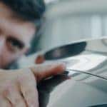 A man is closely inspecting a black car.