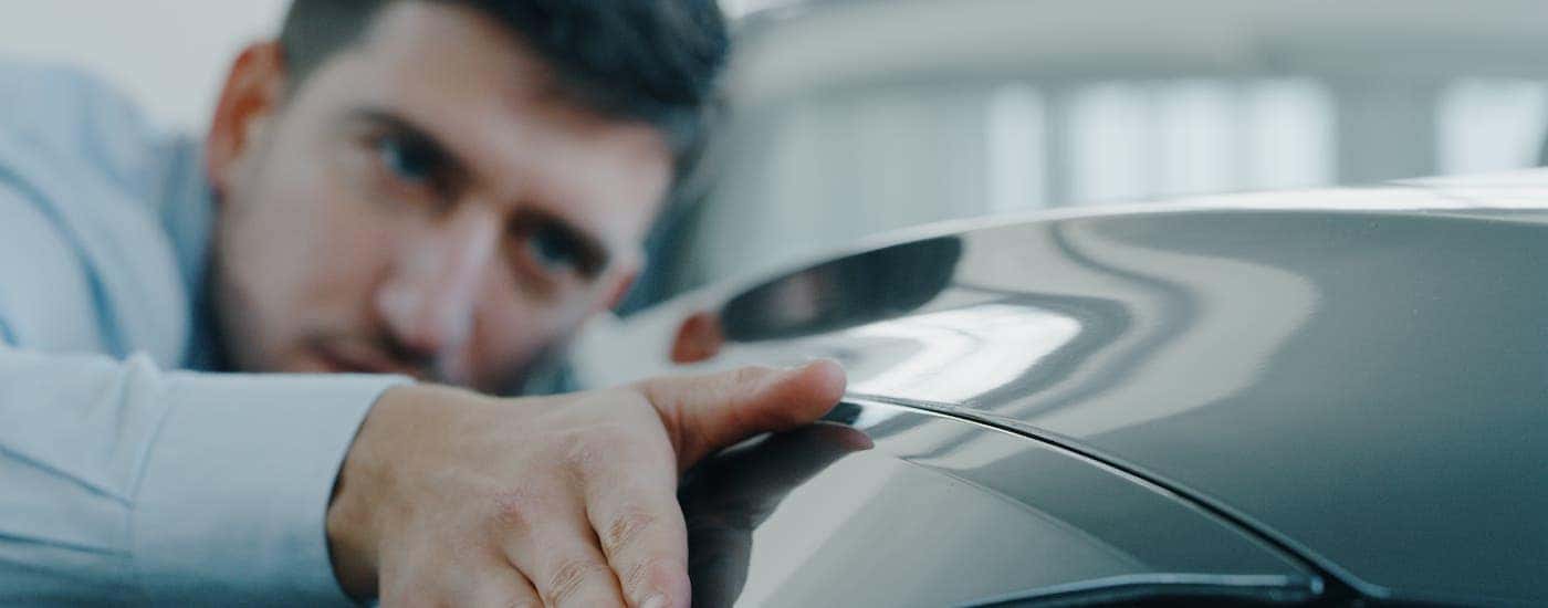 A man is closely inspecting a black car.
