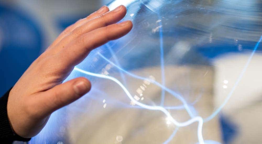 A child's hand is touching a shere wwith blue waves of electricity moving inside.