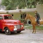 A red 1948 Ford F-1 is shown with two men leaning against it and a man on horseback next to it.