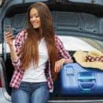 A girl is leaning against an open car trunk with bags.