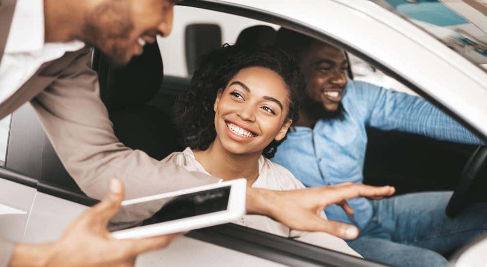 A salesman is talking to a couple sitting in a car.