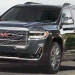A grey 2021 GMC Acadia is driving past a body of water.