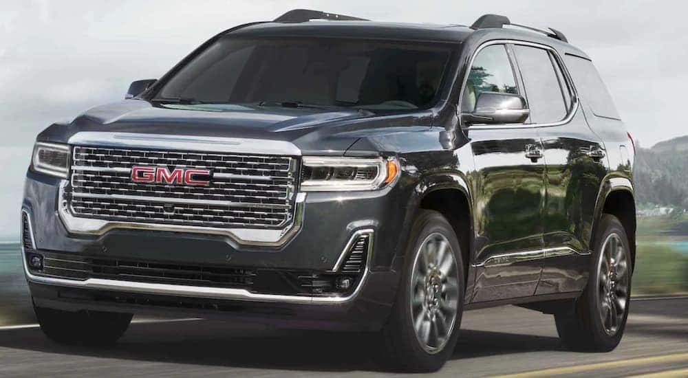 A grey 2021 GMC Acadia is driving past a body of water.
