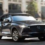 A grey 2021 Mazda CX-5 is driving around a corner on a city street.