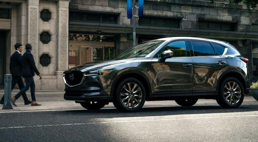 Two people are walking toward a grey 2021 Mazda CX-5 on a city street after leaving an Indiana, PA, Mazda dealer.