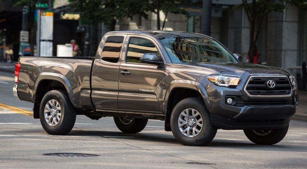 A popular used Toyota Tacoma for sale, a gray 2020 model, is driving on a city street.