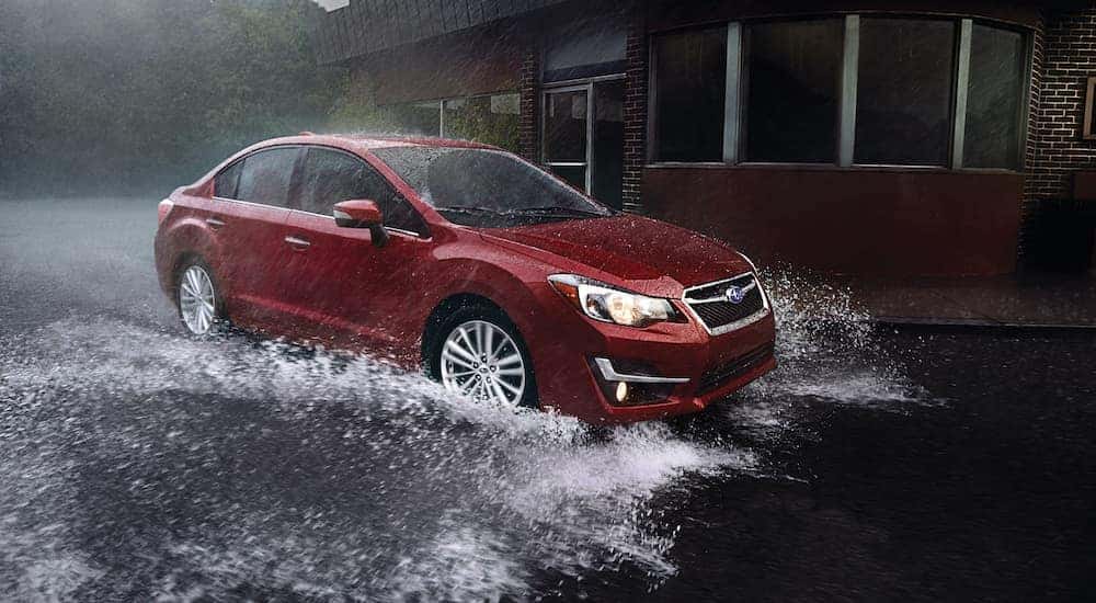 A red 2016 Subaru Impreza 2.0i Limited is shown splashing through a large puddle.