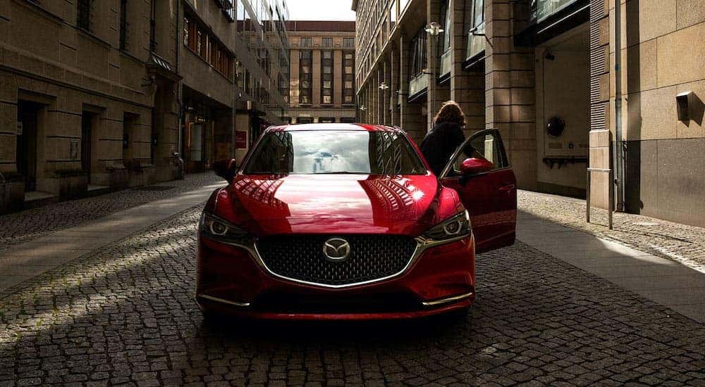 A red 2020 Mazda 6 is shown from the front parked on an empty street in the city.