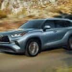 A blue 2020 used Toyota Highlander is driving past a forest after leaving a used SUV dealership.
