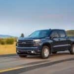 A blue 2019 Chevy Silverado 1500, which is popular among used trucks near me, is driving on a rural road.