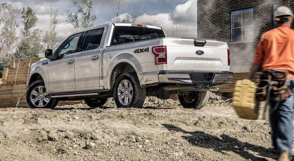 A worker is walking toward a silver 2020 Ford F-150 at a construction site.