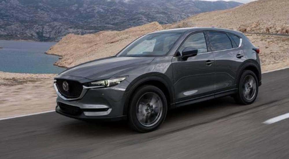 A grey 2020 Mazda CX-5 is shown driving past a lake.