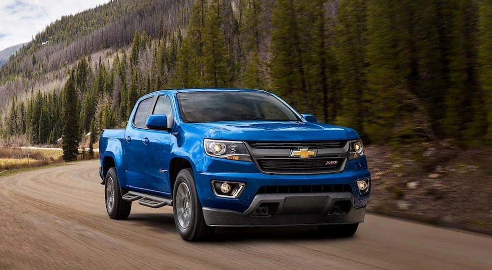 A blue 2020 Chevy Colorado Z71 is shown driving down a dirt road past a forest.