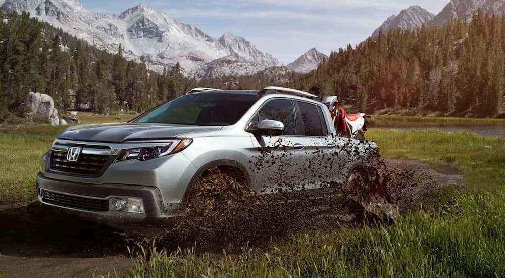 A silver 2020 Honda Ridgeline RTL-E is shown off-roading through a muddy field.