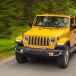 A yellow 2021 Jeep Wrangler is driving down the street past blurred woods after leaving a Jeep dealer near you.