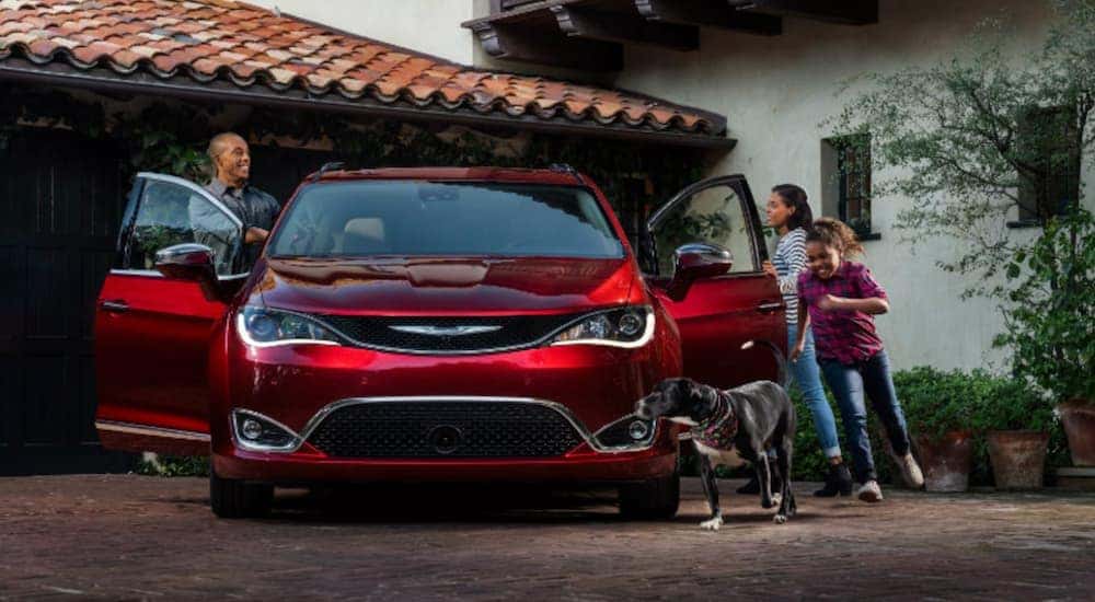 A red 2018 Chrysler Pacifica is parked in a drivway as a family and dog get out.