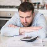 A man is sitting with his arms crossed in front of paperwork.