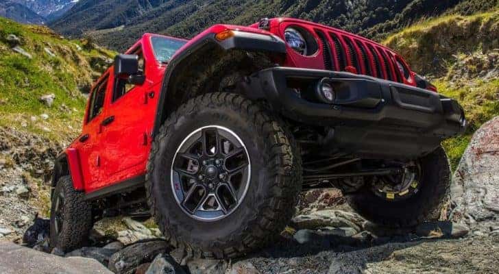 A red 2021 Jeep Wrangler Unlimited is shown from a low angle parked on a rock pile.