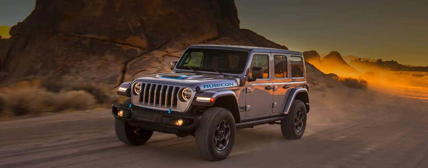 A silver 2021 Jeep Wrangler Rubicon 4xe is shown driving on an open road at dusk after leaving a Jeep Wrangler dealership.