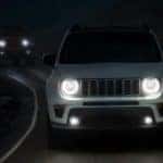 A white 2020 Jeep Renegade is shown at night with its smart headlights illuminated after leaving a used car dealership in Lexington.