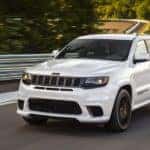 A white 2020 used Jeep Grand Cherokee Trackhawk is shown driving past a guard rail.