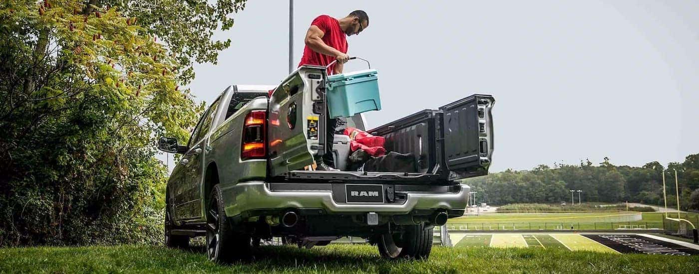 A person is shown loading a gear into the bed of a silver 2024 Ram 1500.