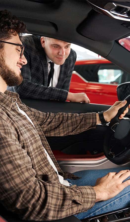 Leasing versus Buying a Hyundai at Delaney Hyundai of Dubois in DuBois, PA | Man sitting in drivers seats of a new car while salesman looks over