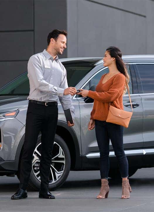 Leasing versus Buying a Hyundai at Delaney Hyundai of Dubois in DuBois, PA | Salesman handing over new car keys to woman in orange shirt