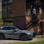 The 2025 INFINITO QX50 Sexy Passenger Side Profile, Parked Outside A Driver's Home. Two People Talk Together On The Stairs To The Home, Speaking Of The Towing Capabilities Of Their Amazing INFINITI SUV