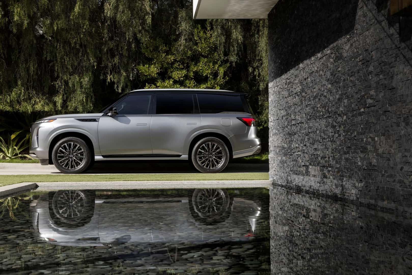 The 2025 INFINITI QX80 Side Profile, Parked Near A Water Pool That Reflects It Majesty And Value