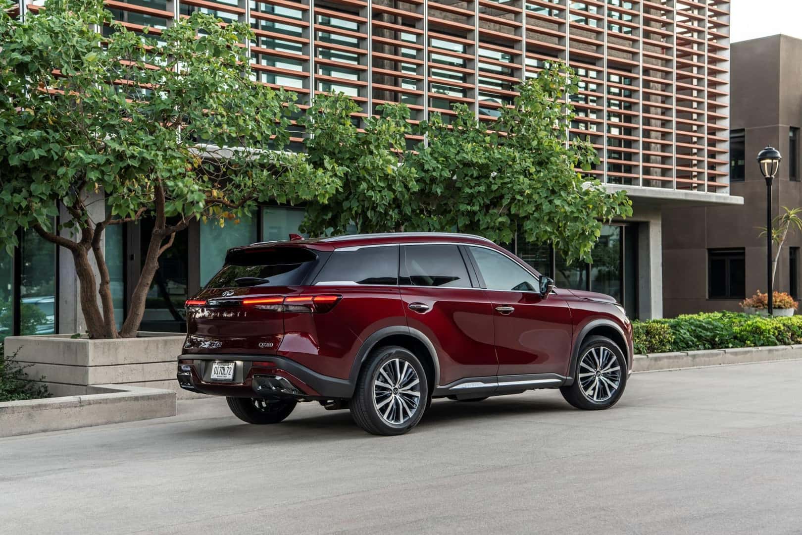 The INFINITI QX60'S Pretty Burgundy Passenger Side, Parked Outside A Luscious And State Of The Art Office Building