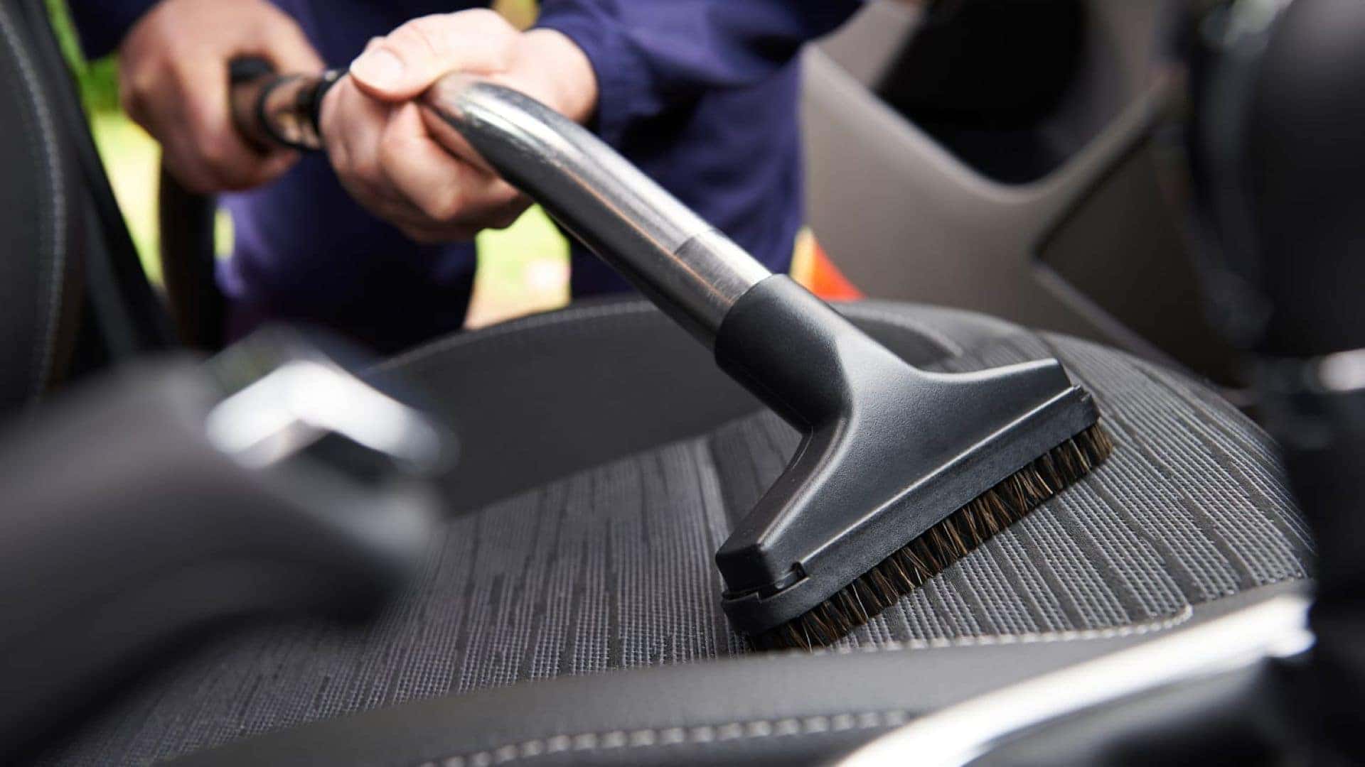 A Car Detail Worker Diligently Vacuuming An Interior