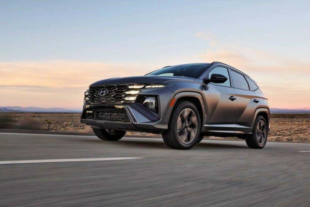 A 2025 Hyundai Tucson driving along a scenic road, showcasing its sleek design and modern features in motion.