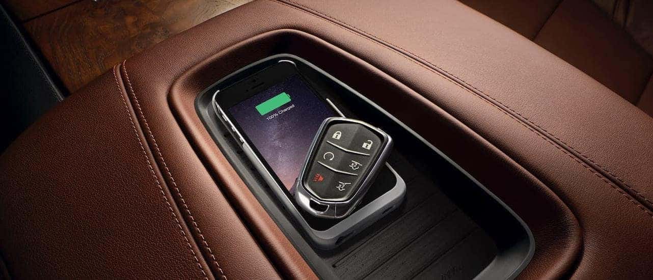 A phone and key fob are shown in the wireless charging pad in a 2020 Cadillac Escalade with brown leather interior. This is some of the technology that helps the Escalade win in the 2020 Cadillac Escalade vs 2020 Chevy Suburban comparison.