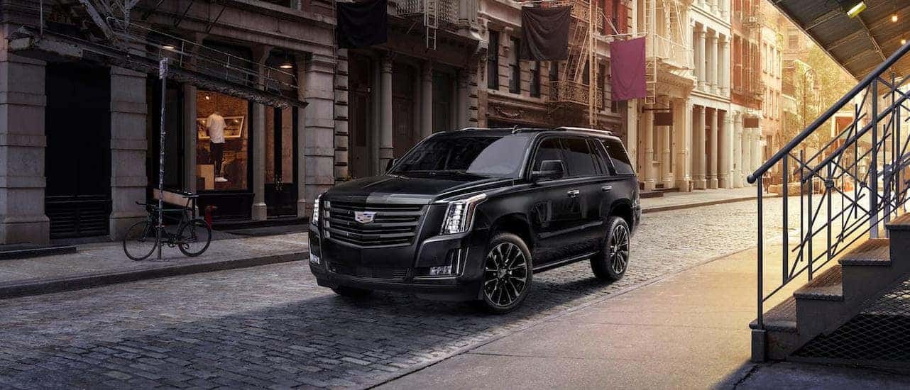 A black 2020 Cadillac Escalade is parked in a cobblestone alleyway at sunset.