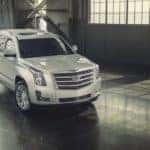 People are standing in front of a white 2017 used Cadillac Escalade that is parked in a warehouse.
