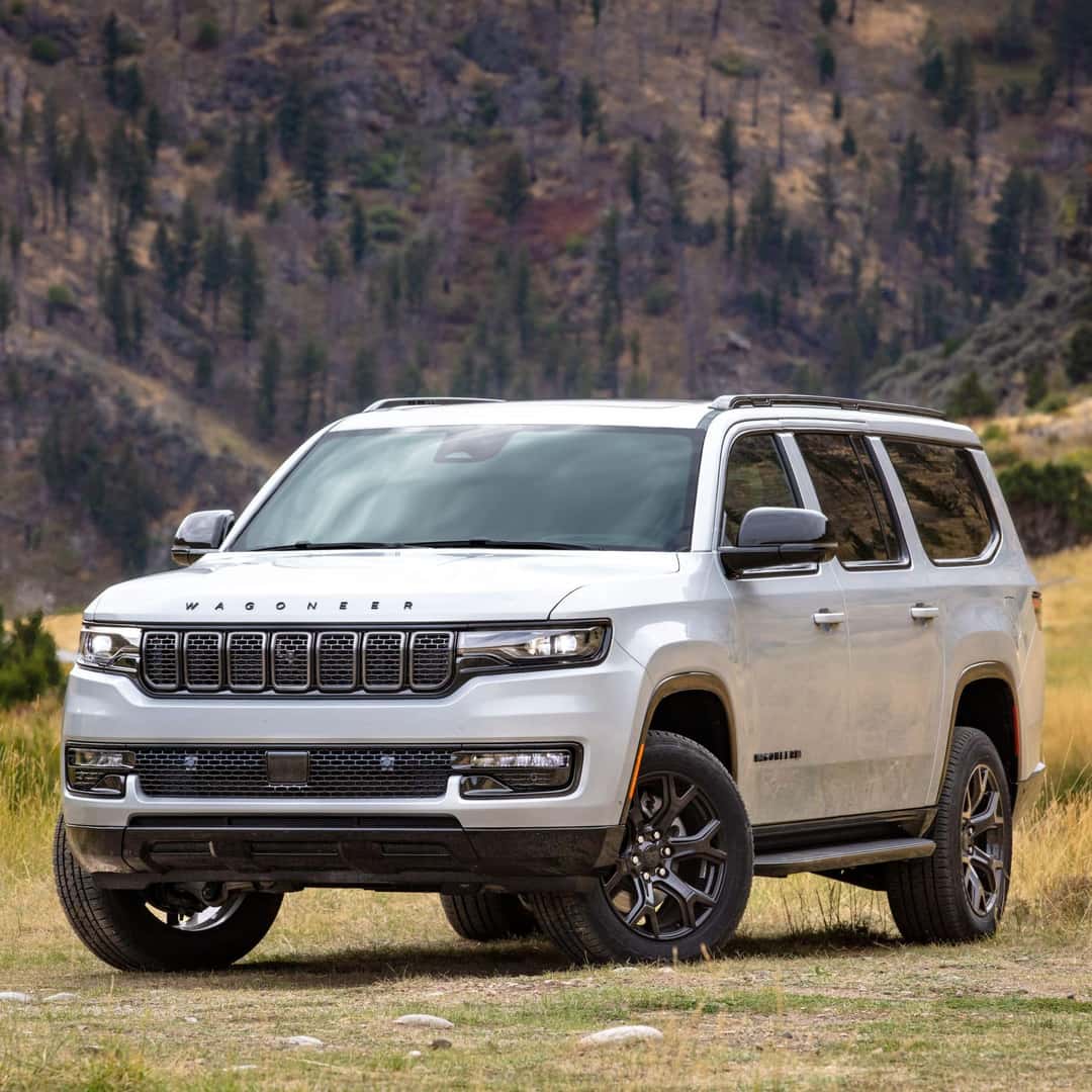 2023 Wagoneer L Series II Carbide in Bright White parked on grass in front of a steep cliffside.