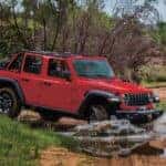 2026 Wrangler Rubicon in Firecracker Red driving into a shallow creek, with tree