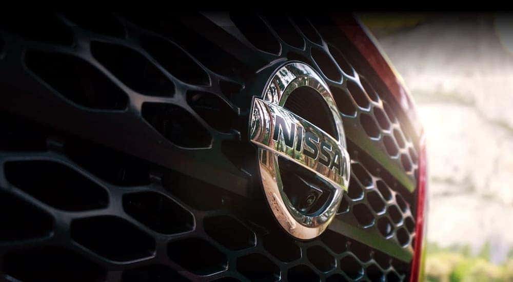 A closeup shows the Nissan badging on a red car's grille.