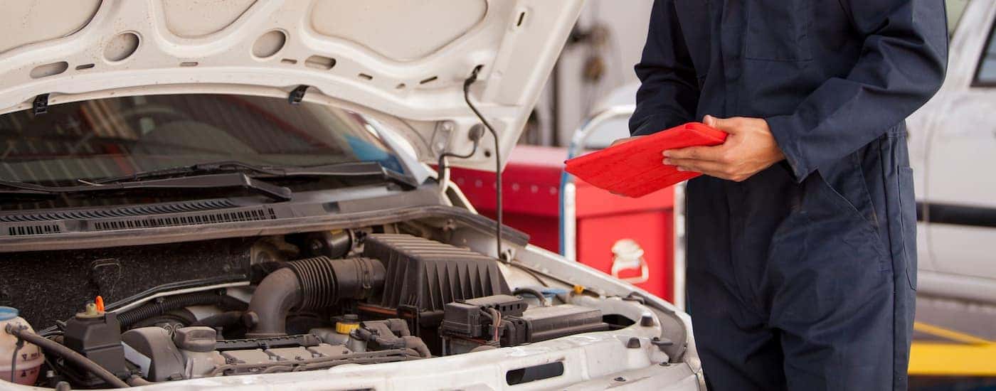 A mechanic holding a clipboard next to a white car is shown.