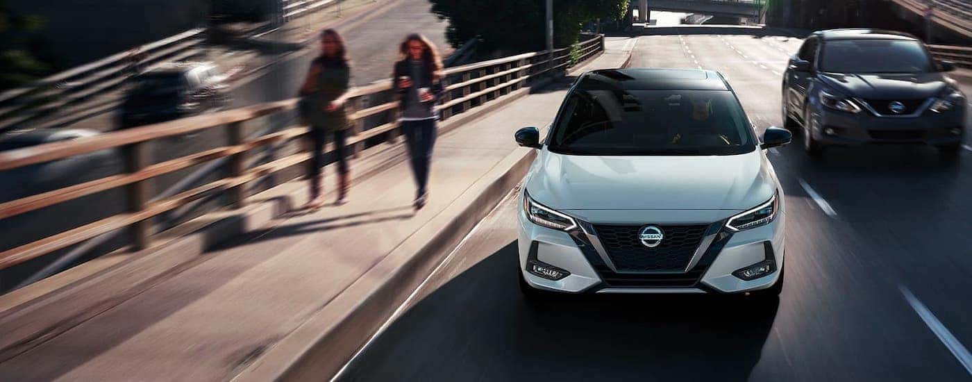 A white 2020 Nissan Sentra is shown from the front driving on a city street.