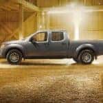A grey 2021 Nissan Frontier is shown from the side, parked in a barn near hay bales.