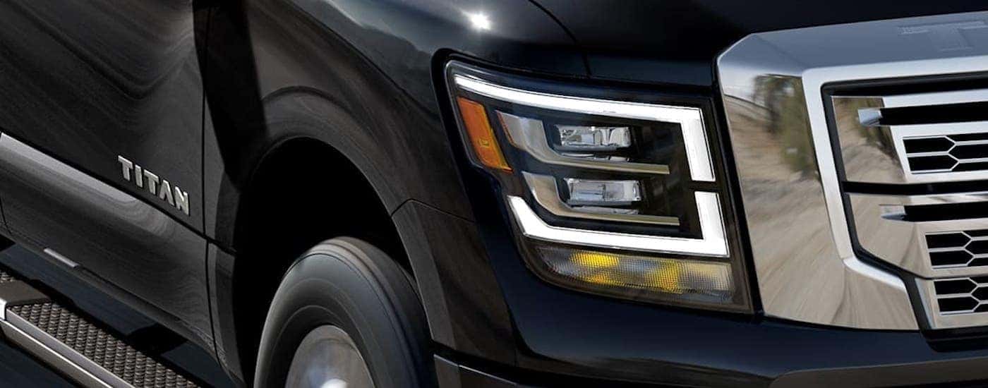 A closeup shows the side badging, headlight, and grille of a black 2021 Nissan Titan at a Shelbyville Nissan Dealer.