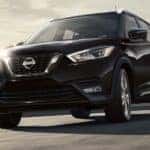 A popular Nissan lease deal, a black 2021 Nissan Kicks, is shown driving on a highway leaving the city.