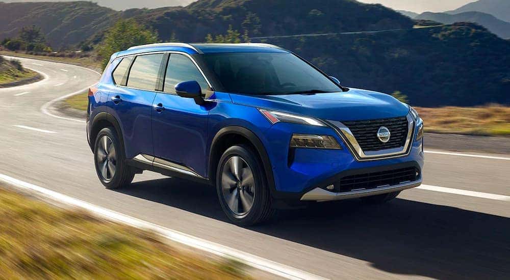 A blue 2021 Nissan Rogue is shown from the side driving down a windy road.