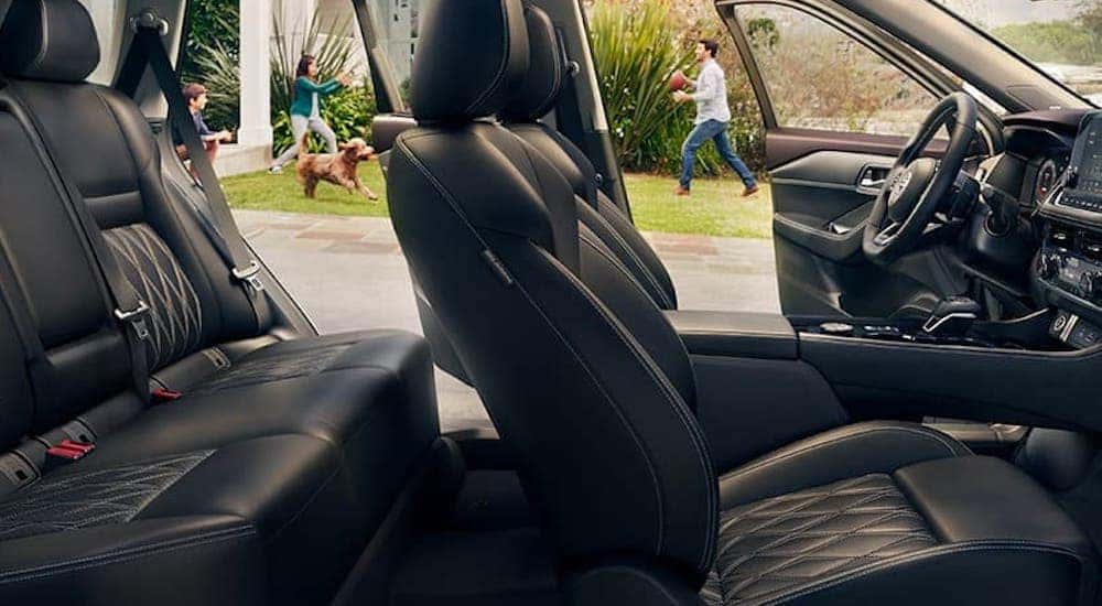 The black interior is shown in a 2021 Nissan Rogue with a family playing catch outside.