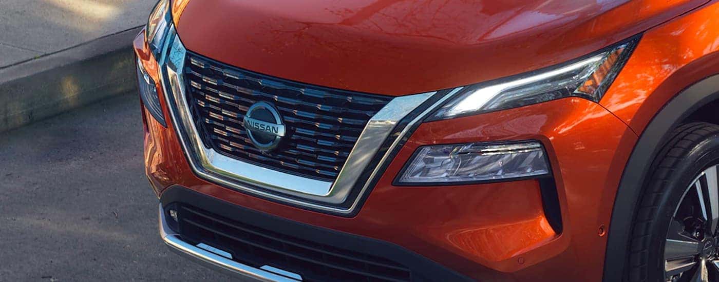 A close up shows the front grille and headlights on an orange 2021 Nissan Rogue.