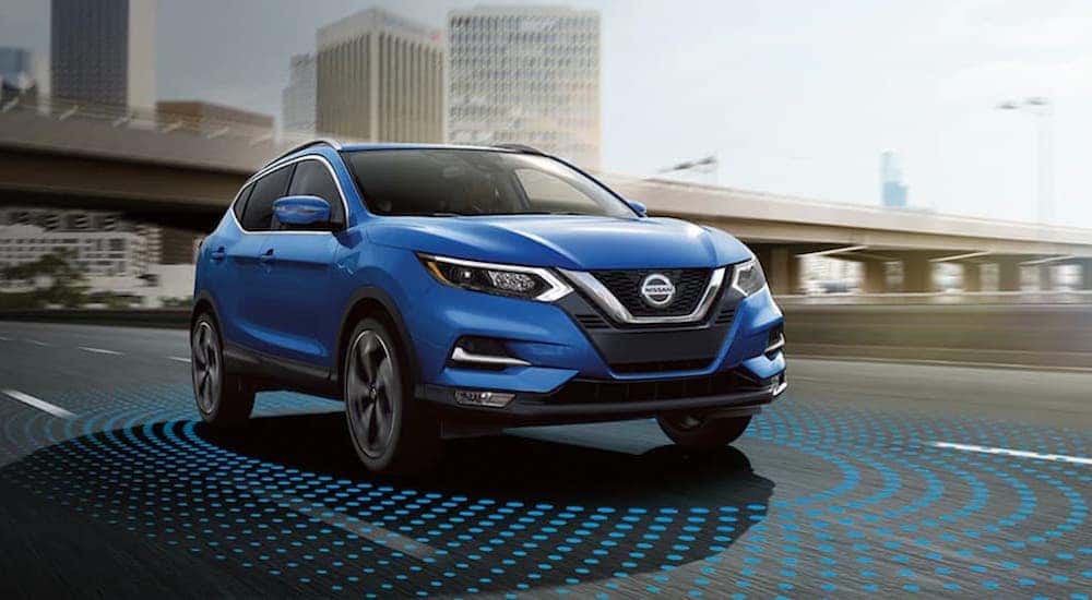 A blue 2021 Nissan Rogue Sport is shown on the highway with simulated safety sensor lines.