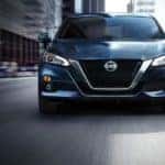 A blue 2021 Nissan Altima is driving through a city after leaving a Nissan Altima dealership.